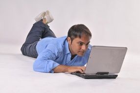 man lying on the ground working at a laptop