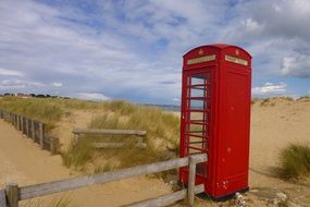 red vintage phone booth on sand beach