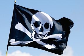 Black and white Pirate flag floating in the wind at blue sky background with white clouds