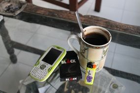 a cup of coffee with cigarettes and a telephone on the table