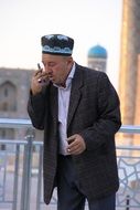 elderly uzbek, muslim man in tubeteika talking on cell phone