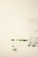 green pills and a glass on a white background