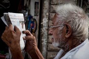 portrait of old man in glasses reading newspaper