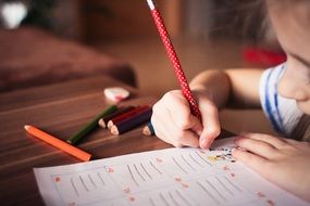 little girl writes in pencil in a notebook