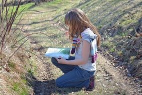 blonde girl reading book on path