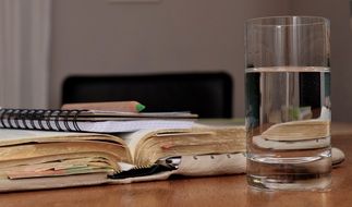glass with water in front of open book on desk