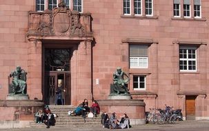 students sit on steps at entrance to university building, germany, freiburg