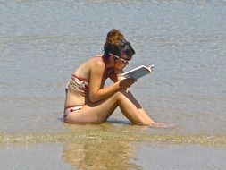 girl with a book in the water on the beach