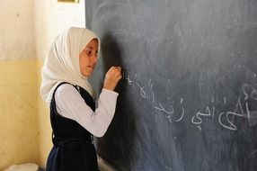 Iranian girl writes with chalk on a blackboard