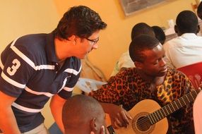 professor stands near a student with a guitar