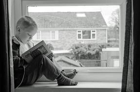 boy sitting on the windowsill with a book