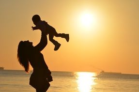 mother with baby on the ocean at sunset