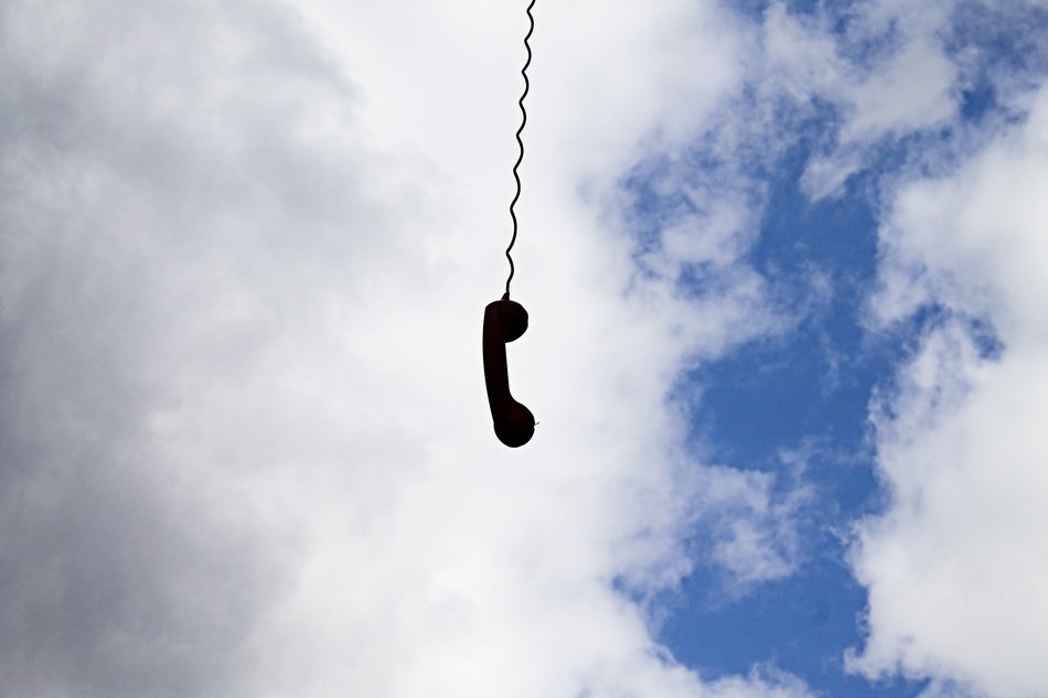 A handset with a cord on the background of the sky with clouds