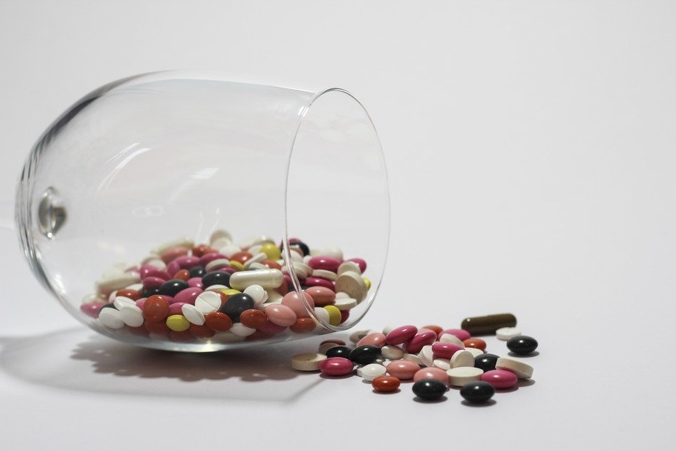 Colorful medications in the glass and on the table on white surface