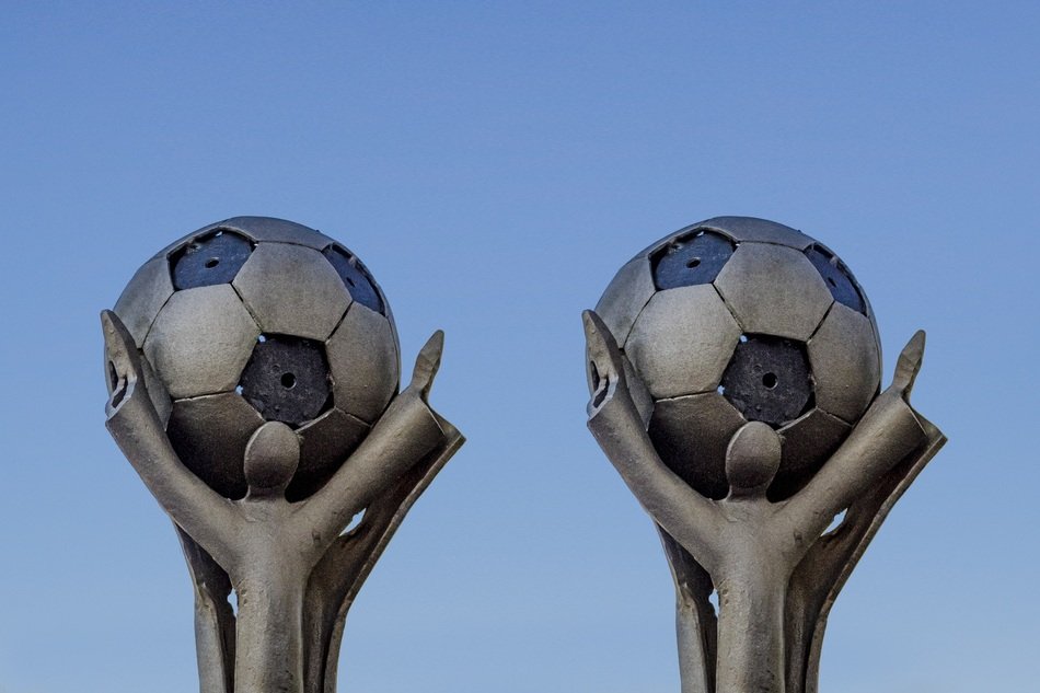 two sculptures of peoples who keep the ball in his hands against the sky