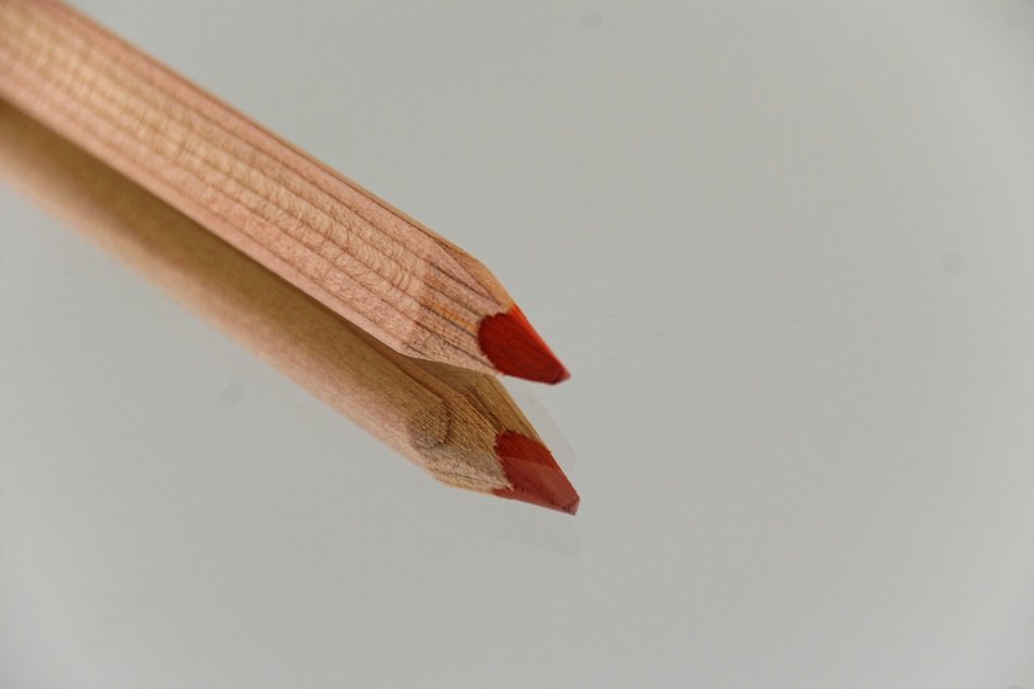 wooden pencil with red core on the background of reflective surface