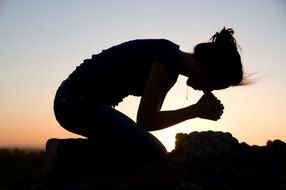 silhouette of a woman praying in nature