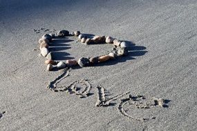 stones arranged in heart form and love word on sand