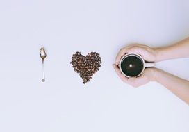 coffee cup in hands spoon coffe beans in shape of heart