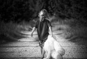 girl drags a white teddy bear along a rural road