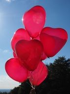 Red balloons in the shape of a heart against a blue sky in the glare of the sun