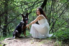 girl in a white dress holds a German shepherd by the paw