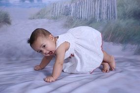 baby in a white dress on white sand