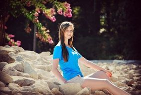 beautiful happy young girl sits on rocks outdoor