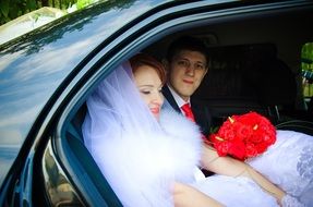 Newlyweds with a red bouquet in a black car