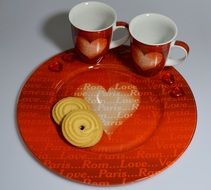 Biscuits on red plate and two red cups with the white hearts