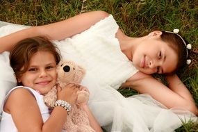 two happy girls with a teddy bear in a meadow