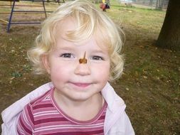 blonde child girl with maple seeds on nose in park at autumn