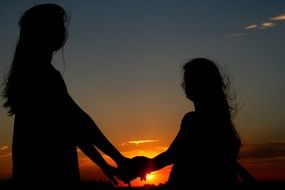 silhouette of two girls holding hands at sunset sky