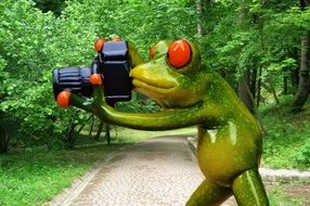 Figurine of a green frog with a camera on a nature background