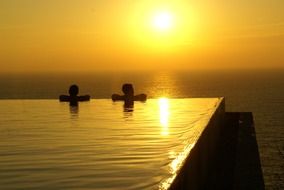 couple in pool at colorful sunset on horizon