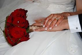 bride and groom hands on red rose wedding bouquet