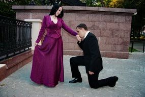 a man kneels in front of a woman and kisses her hand