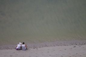 man and woman sitting on beach sand