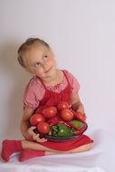 girl with plate of colorful vegetables at white wall background