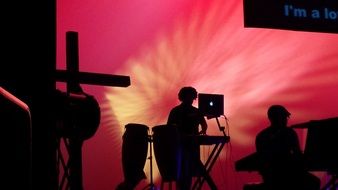 silhouettes of cross and musicians on stage