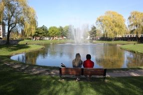 friends sit on a bench near the lake among the plants