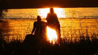 silhouettes of people on the lake from sunset