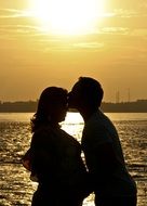 A kiss of a man and a pregnant woman at sunset