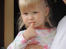 girl with blue eyes holds a finger in her mouth