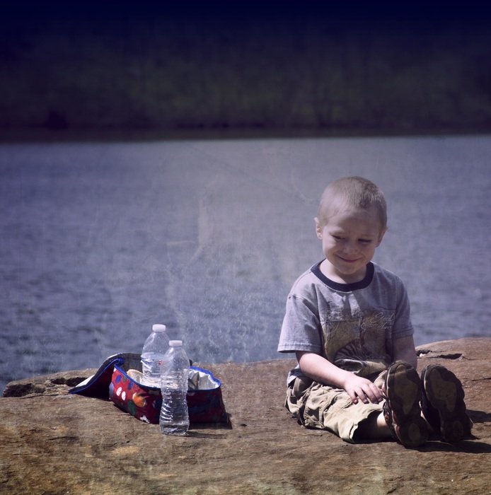 happy boy sits at picnic box near lake