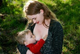 Caucasian mom breastfeeding baby outdoorÑ