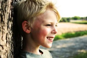 happy boy with white hair stands near a tree