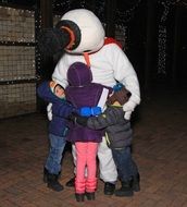 children hug a man in a snowman costume