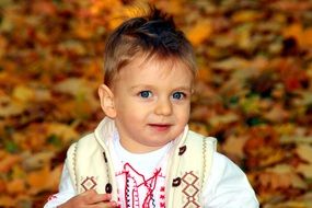 a smiling child with blue eyes on a background of yellow autumn leaves