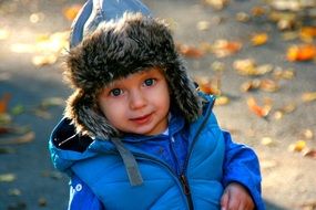 blue-eyed baby in blue jacket on a background of yellow leaves